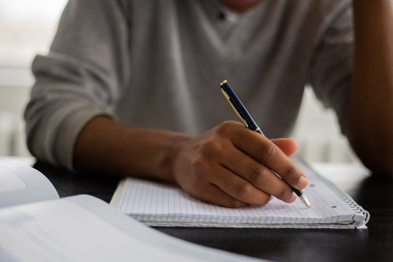 Close-up of a student writing notes in a notebook with a pen, emphasizing academic focus.